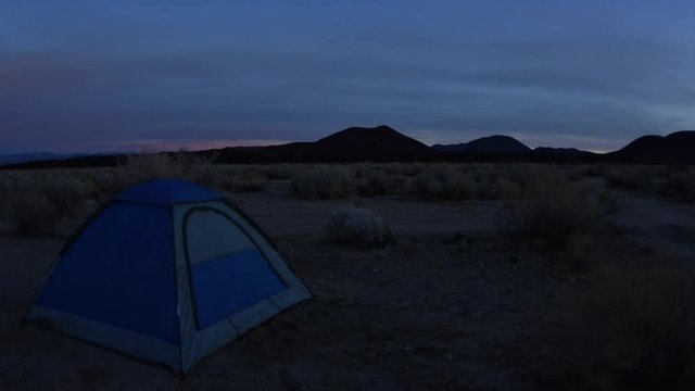 Wide angle time lapse arriving dawn as first light appears across rugged Mojave desert landscape and revfeails camping tent