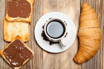 cup of coffee, croissant, toast and chocolate on wooden table