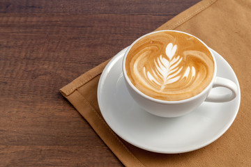 Coffee cup of rosetta latte art place on napkin on wooden backgr