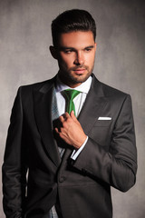 portrait of sexy young man in tuxedo correcting his tie