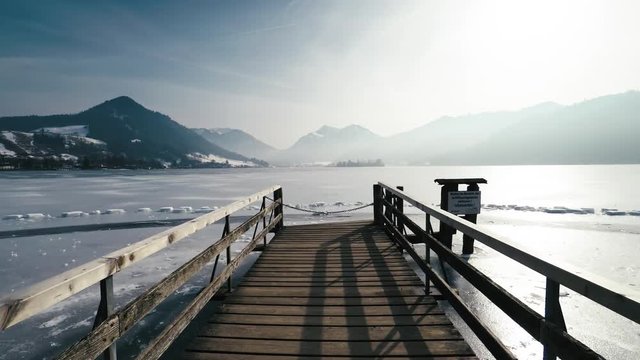 Pov shot of walking on a wooden jetty over frozen lake schliersee against mountains