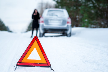 A picture of a young woman having a problem with a car on a wint