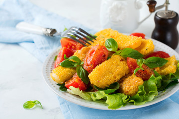 Fried cheese slices in corn grits, cooked tomatoes and lettuce on a light background. breakfast concept. Selective focus.