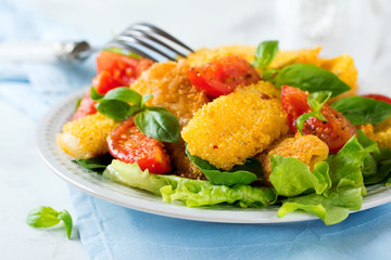 Fried cheese slices in corn grits, cooked tomatoes and lettuce on a light background. breakfast concept. Selective focus.