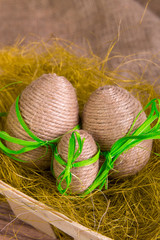 Easter eggs wrapped in twine in yellow nest on wooden sackcloth wooden background. Rustic style.