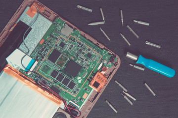 Process of PC Tablet device repair near screwdriver and bit on black wooden background. Top view....