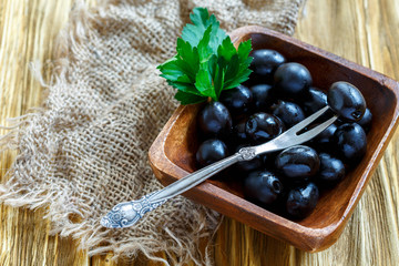 Black olives and fork in a wooden bowl.