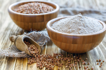 Scoop with buckwheat and buckwheat flour in a wooden bowl.