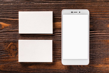 Mockup of cellphone and two business cards at brown wooden board