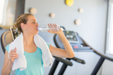 Young woman drinking water in gym room