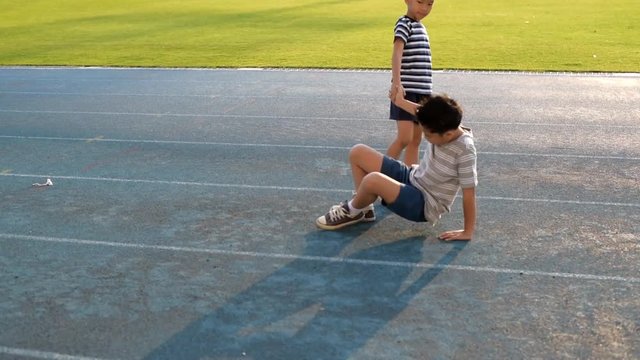 Young Asian boy running on blue track, fall and help by another boy.