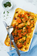 Baked pumpkin with chicken, spices and cream sauce in a white ceramic form on a light background. Selective focus.Top view.