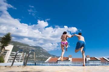 Couple man and woman holding hands jumping in swimming pool