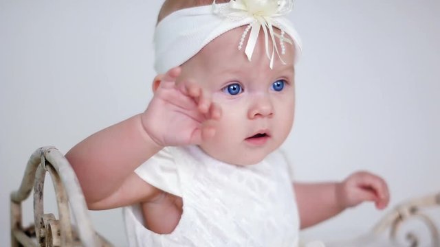 baby girl in white dress and headband sitting on a little iron bed