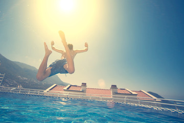 Man in blue shorts jumping in swimming pool on the roof at sunny day