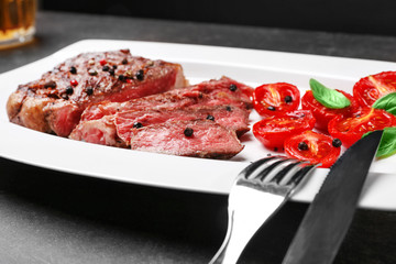 Sliced tasty steak with spices and tomatoes on white plate