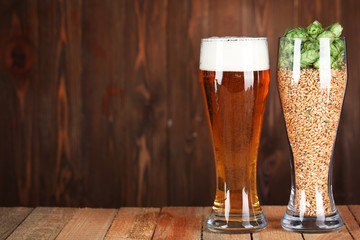Glasses with beer, hops and malts on wooden background