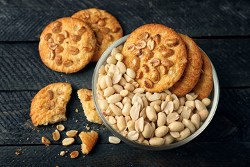 Peanut cookies and bowl with nuts on wooden table