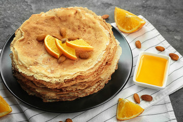 Stack of delicious pancakes with orange and nuts on black plate