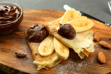 Delicious pancakes with banana and chocolate on wooden board