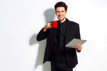 Young businessman smiling in the morning on a white background. dressed in a suit. coffee and gadget in their hands. concept business. excellent mood.
