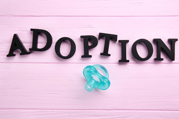 Word ADOPTION and passifier on color wooden background