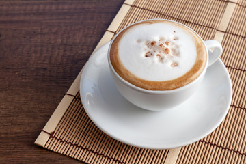 Coffee cup of cappuccino on bamboo mat, on wooden background wit