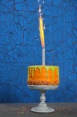 Tasty birthday cake with firework on colorful wooden background