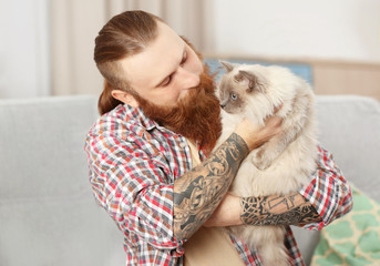 Young bearded man with fluffy cat sitting on sofa