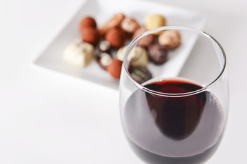 Glass of red wine and delicious chocolate candies on white background