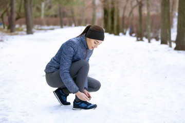 Fototapeta na wymiar Young woman tying shoelaces in winter park