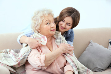 Beautiful girl covering grandmother with blanket on couch at home
