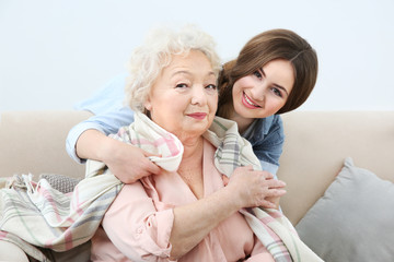 Beautiful girl covering grandmother with blanket on couch at home