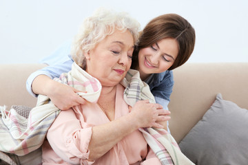 Beautiful girl covering grandmother with blanket on couch at home