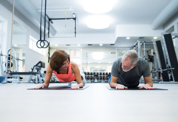Senior couple in gym in plank position working abs