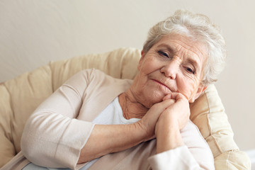 Depressed elderly woman sitting on lounge at home