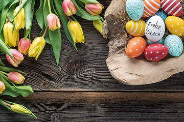 Osternest mit bunten Eier und Tulpen auf altem Holz