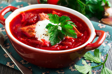 Beetroot soup with meat, sour cream and parsley in a brown ceramic bowl on the old wooden background. Borsch- traditional dish of Ukrainian cuisine. Selective focus.