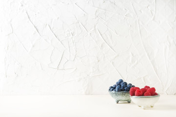 Ripe blueberries and raspberries in a bowl of light. White backg