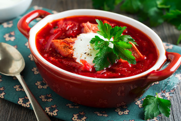 Beetroot soup with meat, sour cream and parsley in a brown ceramic bowl on the old wooden background. Borsch- traditional dish of Ukrainian cuisine. Selective focus.