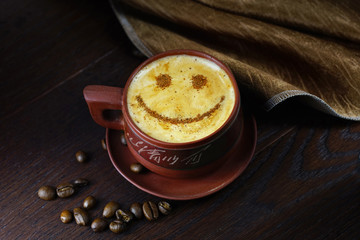 A cup of coffee with smile on brown wooden table close-up. Coffee beans scattered on the table. Beautiful original art composition cheerful image.