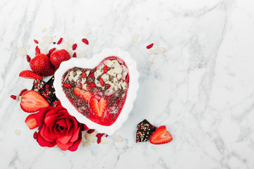 Strawberry smoothie in a bowl in the shape of a heart with copy space. Healthy and tasty breakfast on marble background