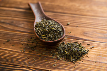 cup of green tea and spoon of dried green tea leaves on wooden background