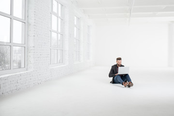 Elegant businessman working with laptop on the floor at the big white office interior