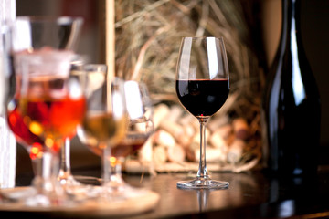tall wine glass filled with red wine, near a dark bottle in the background wine box with wine corks