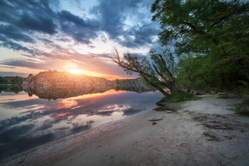 River against colorful sky with clouds and rocks at sunset in summer. Beautiful landscape with lake, mountains, sunlight and blue cloudy sky reflected in water at twilight. Nature. Reflection in water