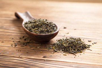 cup of green tea and spoon of dried green tea leaves on wooden background