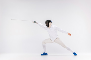 Man wearing fencing suit practicing with sword against gray