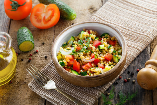 Couscous with tomatoes, cucumber and onion in a bowl for healthy breakfast. Traditional Israeli food Ptitim with vegetables. Moroccan cuisine meal. Top view.