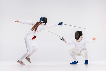 The men and woman wearing fencing suit practicing with sword against gray